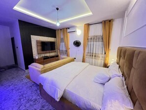 A modern bedroom with a bed, a TV mounted on the wall, and a ceiling light.