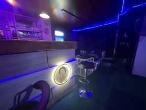 Un espace bar avec un panneau lumineux au néon, un comptoir et des tabourets.