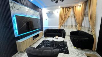 A modern living room with a flat-screen TV, black sofas, a coffee table, and a marble-patterned floor.