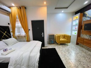 A hotel room with a bed, a desk, a chair, a wardrobe, and a door. - MAGS RESIDENCE (Asubi)