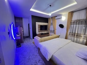 A hotel room with a bed, a television, a ceiling light, and a wall-mounted air conditioning unit.