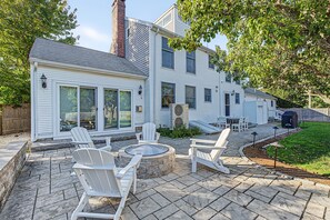 Une maison à deux étages dotée d’un patio aménagé avec des meubles d’extérieur et un foyer.