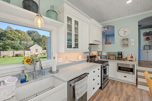A kitchen with white cabinets, a built-in oven, a dishwasher, and a window with a view of a house and trees. - New to our 2027 Inventory!   Spacious 2700 sq. ft.  home with heated pool! (West Yarmouth)