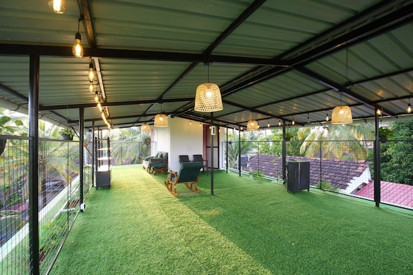 A covered outdoor area with artificial grass, seating, and hanging lights.