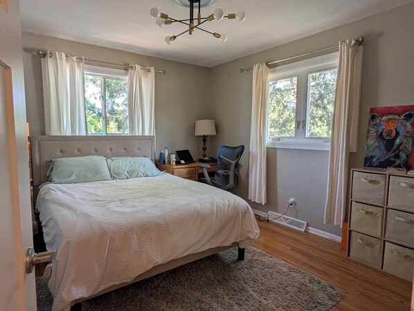 A bedroom with a bed, a desk, a chair, a lamp, and a painting on the wall. - Amazing central location across from CU Boulder (Boulder)