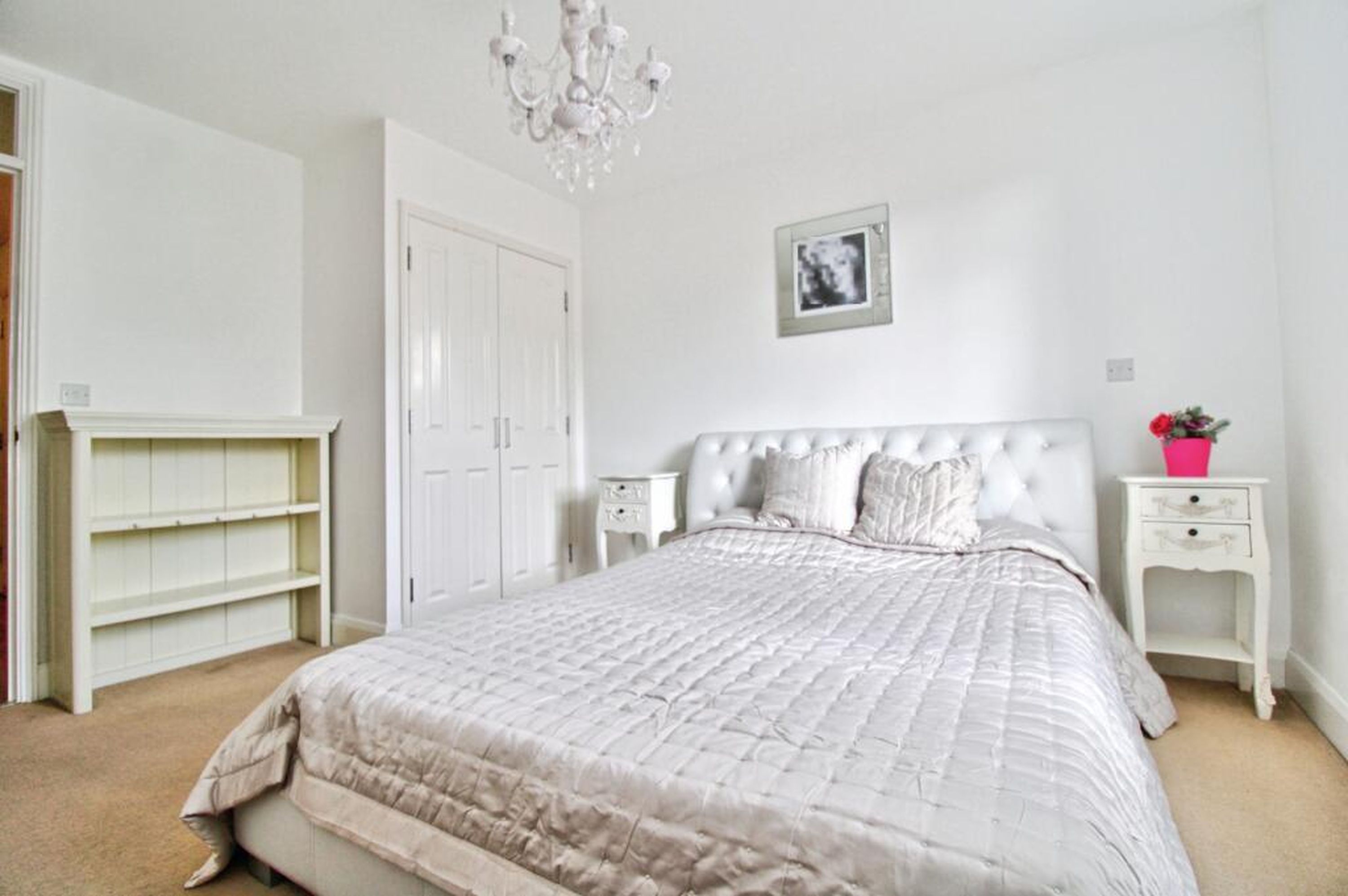 A bedroom with a large bed, a wardrobe, a nightstand, a small table, and a chandelier.
