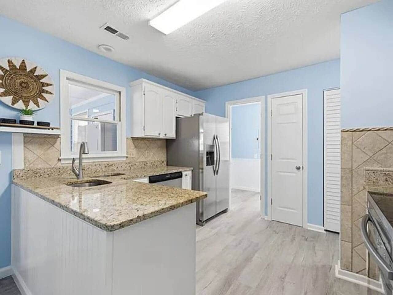 A kitchen with white cabinets, a granite countertop, and a stainless steel refrigerator.