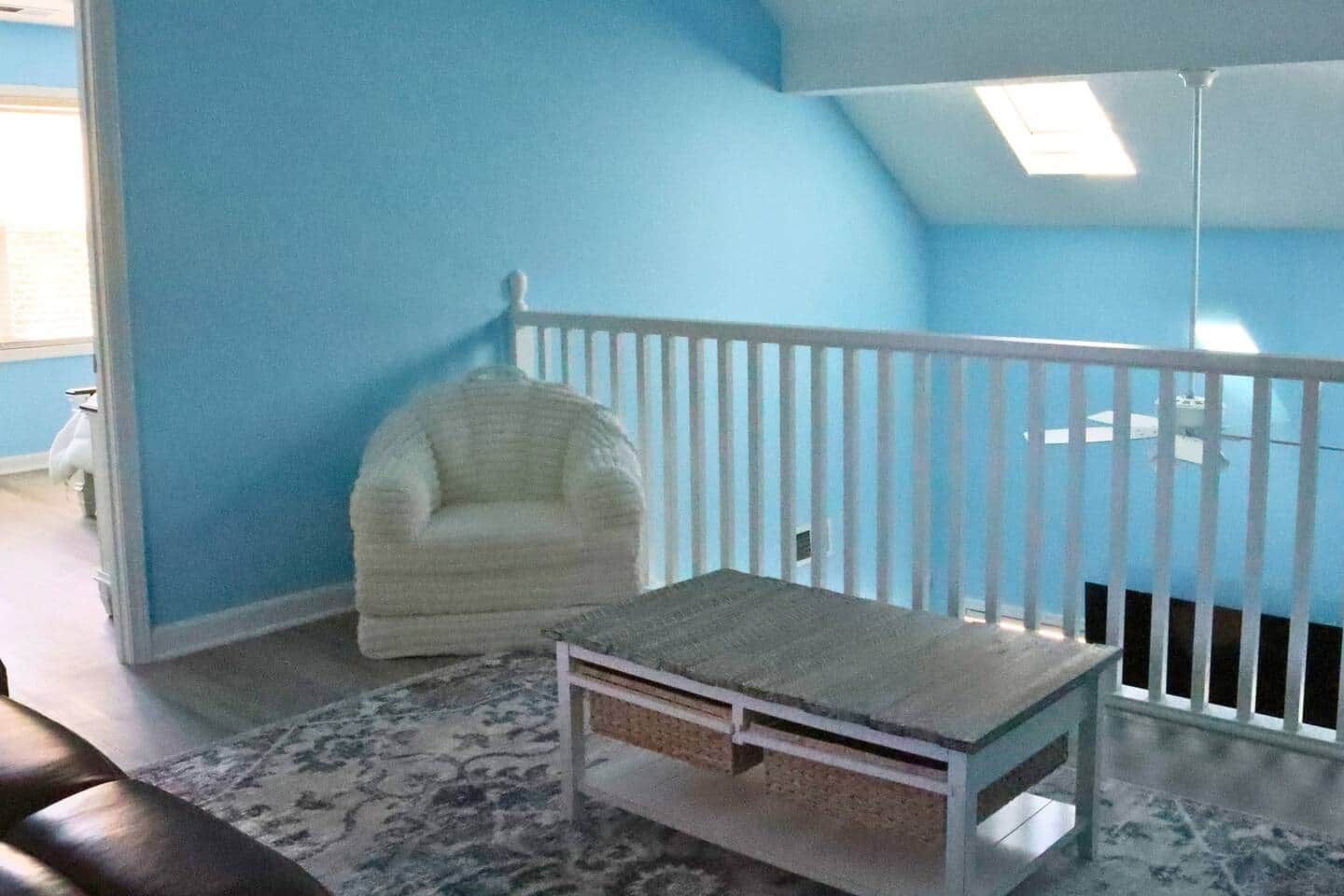 Une pièce avec une chaise blanche, une petite table et une rambarde blanche.