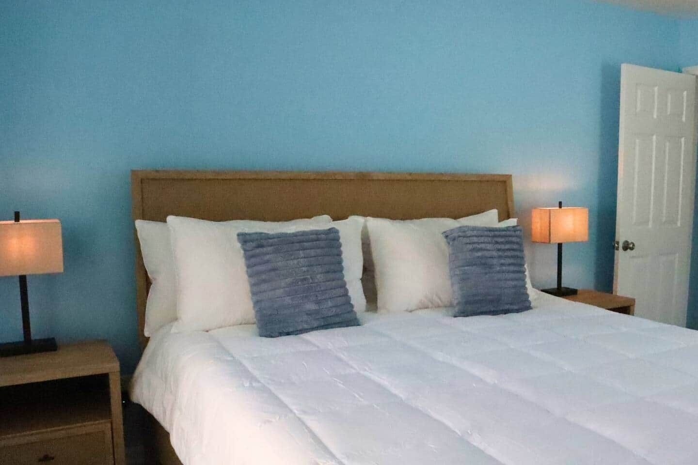 A bed with a wooden headboard, two bedside lamps, and a white door.