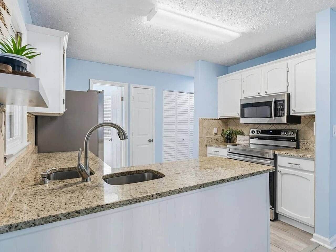 A kitchen with a granite countertop, stainless steel appliances, and white cabinetry.