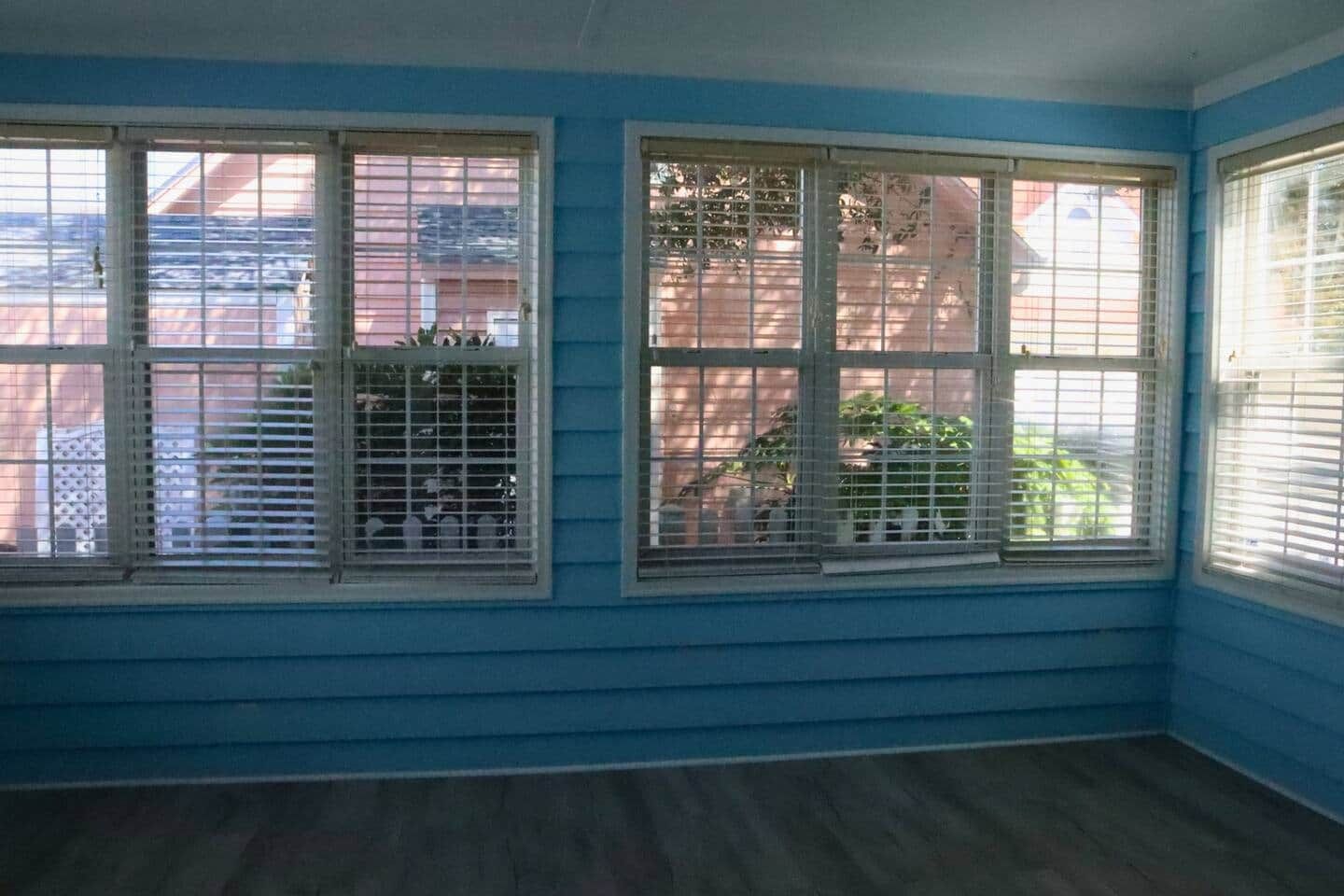 Une pièce dotée de deux fenêtres, d’un plancher en bois et donnant sur un quartier résidentiel.