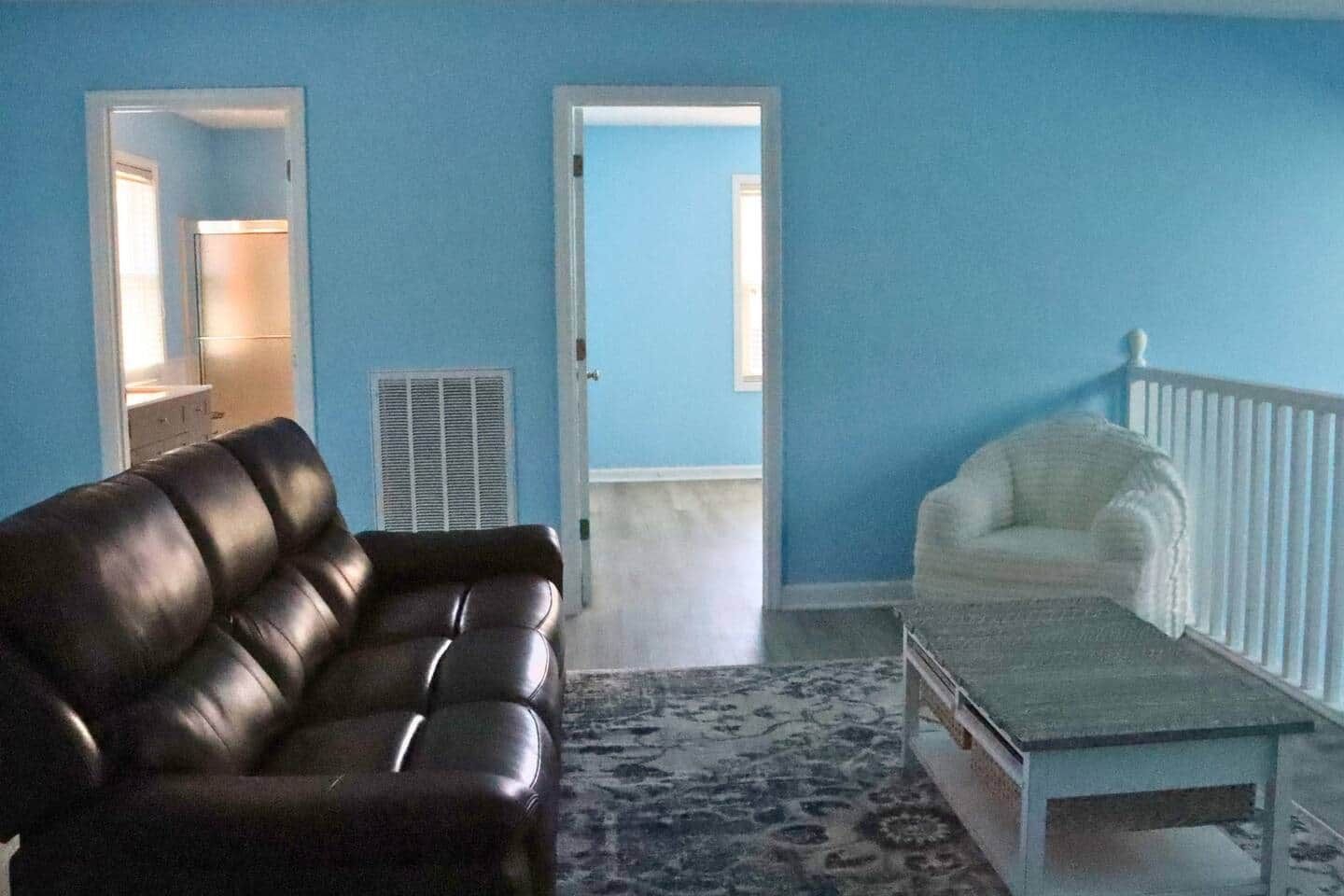Ein Wohnzimmer mit einem braunen Ledersofa, einem weißen Sessel und einem Couchtisch. Auf dem Boden liegt ein gemustertes Teppich.