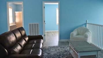 Ein Wohnzimmer mit einem braunen Ledersofa, einem weißen Sessel und einem Couchtisch. Auf dem Boden liegt ein gemustertes Teppich.