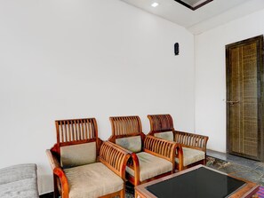 A seating area with three wooden chairs and a small table, a door, and a light fixture on the wall. - Collection O Infopark Kochi (Kanayannur)
