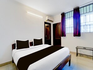 A hotel room with a bed, a bedside table, a window with curtains, and an air conditioning unit. - Collection O Infopark Kochi (Kanayannur)