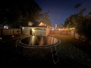 Un trampoline rond se trouve dans un jardin, avec une maison en arrière-plan.