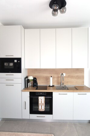 A modern kitchen with white cabinets, a wooden countertop, a built-in oven, a coffee maker, and a sink. - Apartment 'Terrace  Makarska' with Sea View, Wi-Fi and Air Conditioning (Makarska)