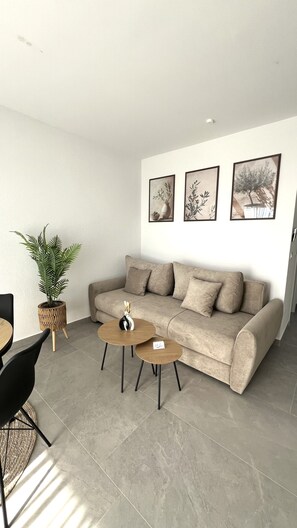 Ein modernes Wohnzimmer mit einem beige farbenen Sofa, zwei runden Couchtischen, einer Topfpflanze und drei gerahmten Bildern an der Wand.