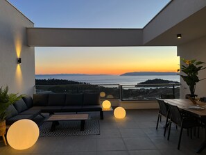 Ein moderner Balkon mit einer Couch, einem Esstisch und Topfpflanzen.