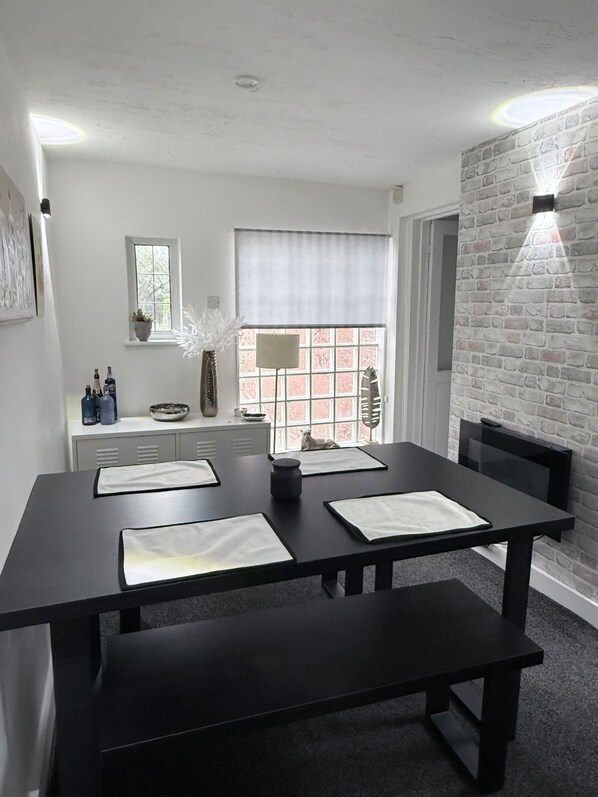 Uma zona de refeições moderna com mesa preta posta para quatro pessoas, um banco, uma janela com vista e uma parede de tijolos.