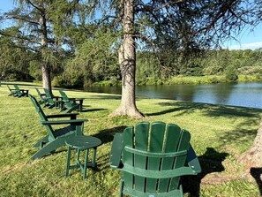 A park with green chairs and tables arranged on grass near a body of water.