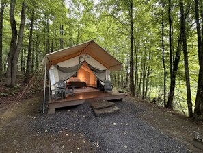Alojamiento en tienda de campaña con cama, zona de estar y vistas al bosque.