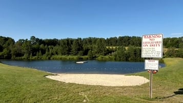 A warning sign near a lake with a clear sky and trees in the background.