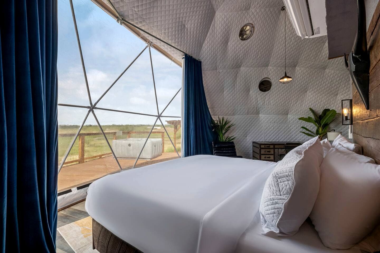 A bedroom with a large bed, a view of the outdoors, and a geometric ceiling design.