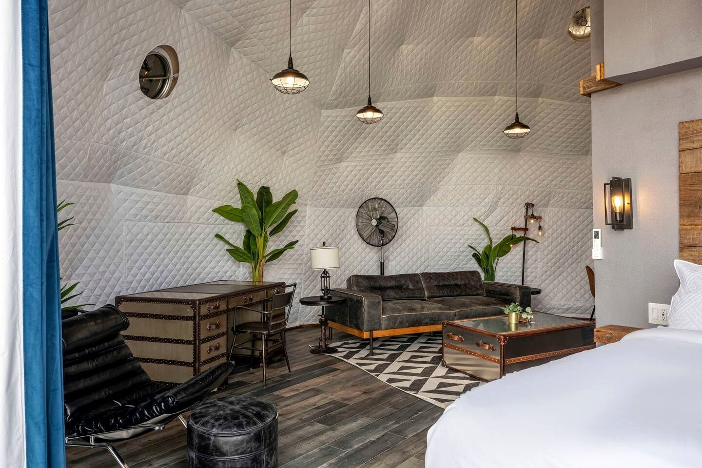A room with a quilted ceiling, a sofa, a coffee table, a desk, and a bed.