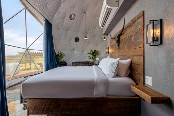 A bedroom with a large bed, a wooden headboard, pendant lights, and a view through a window.