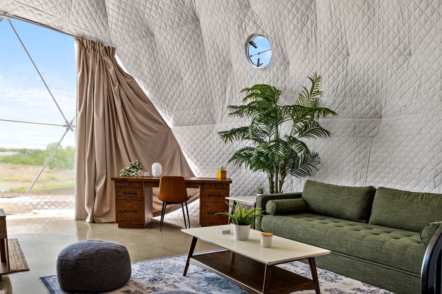 A tented accommodation with a desk, chair, sofa, and potted plants.