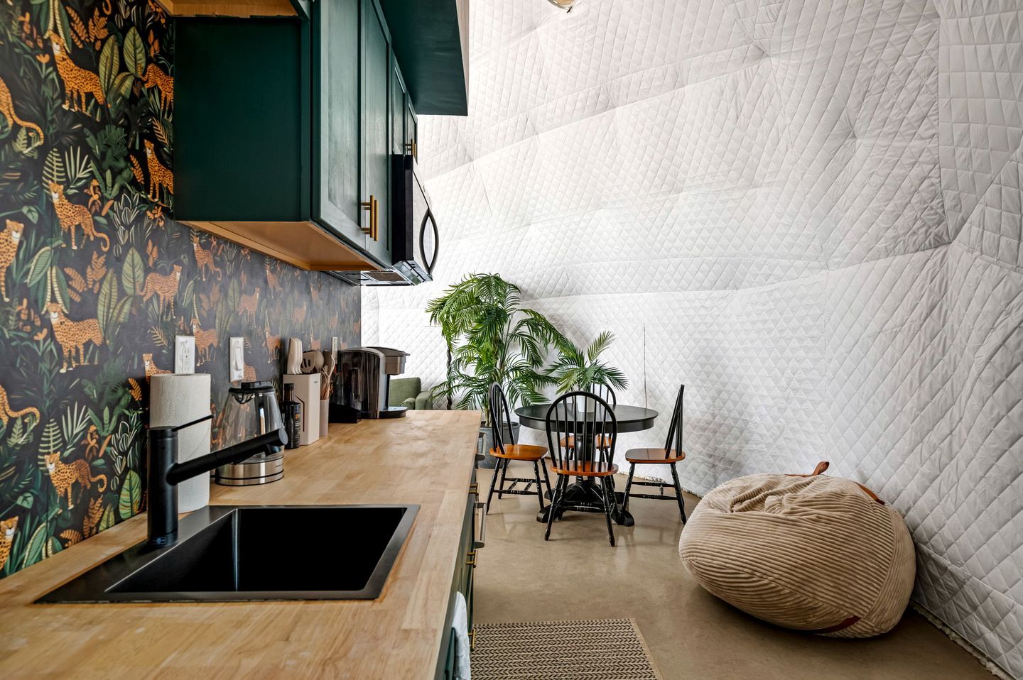 A modern kitchen with a wooden countertop, a sink, and a dining area with chairs and a table.