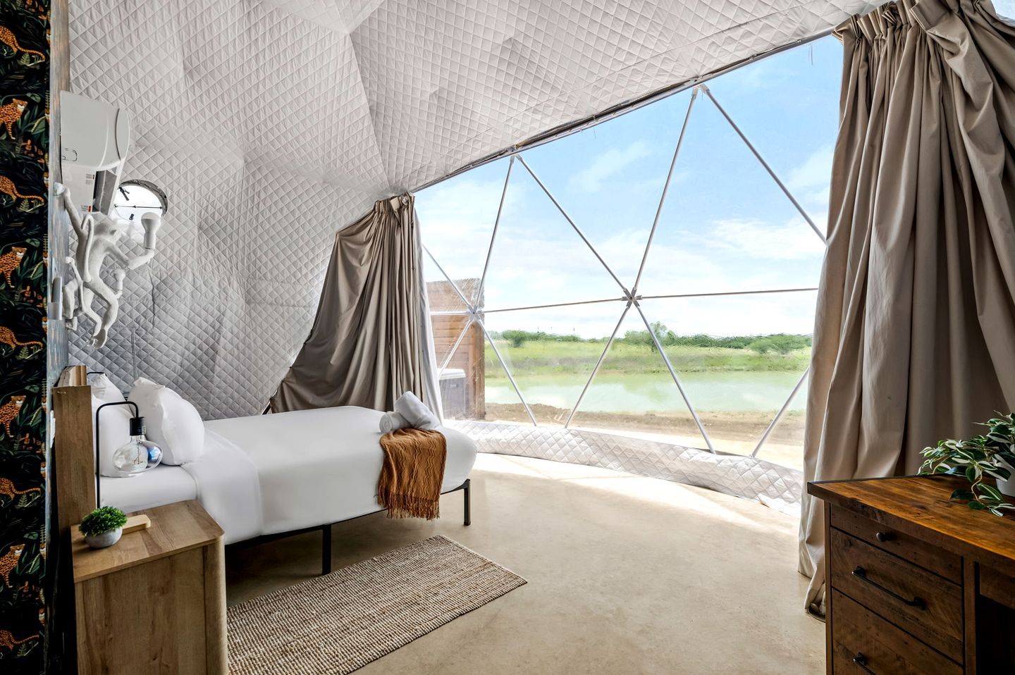 Ein Schlafzimmer mit Bett, Nachttisch, Lampe und Blick auf ein Gewässer durch ein großes Fenster.