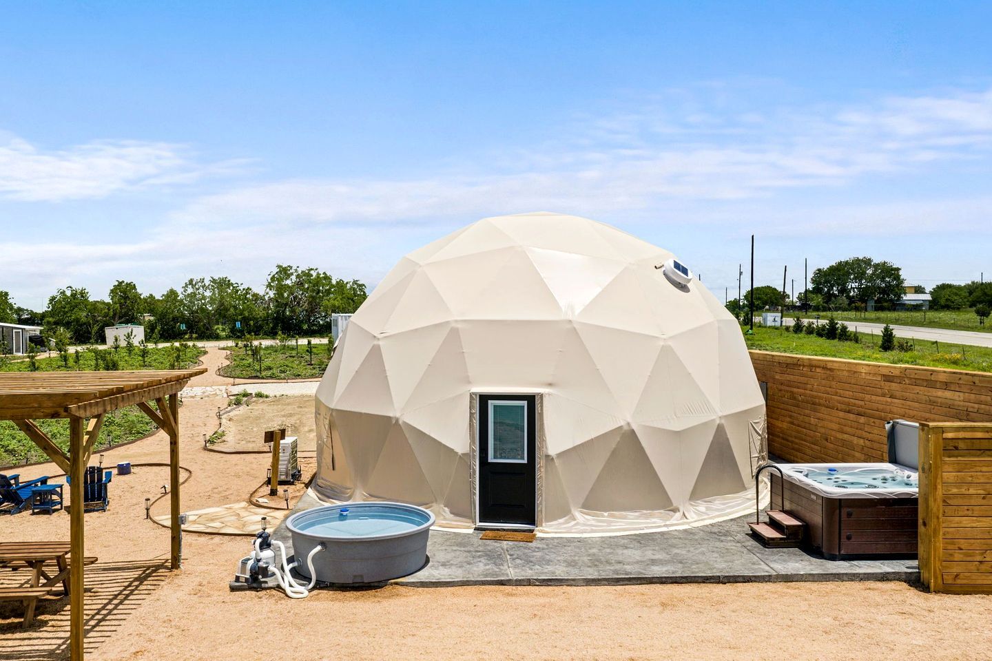 A geodesic dome structure with a door, a hot tub, and a picnic table.