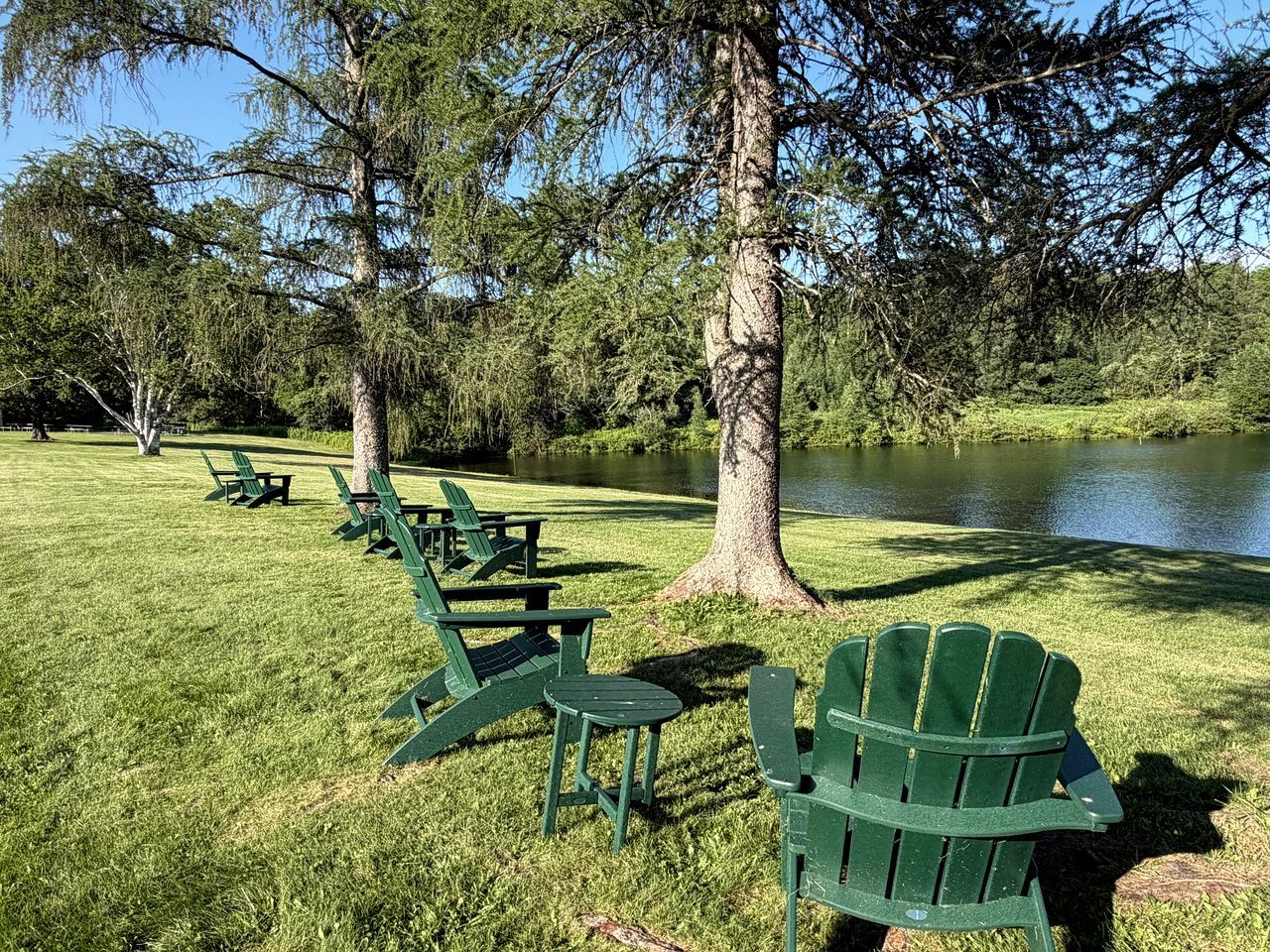 Un parque con sillas Adirondack verdes y un lago.