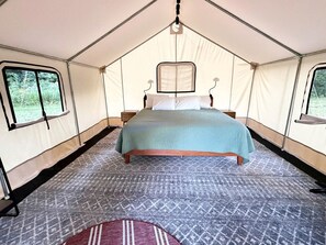 A tent with a bed, two bedside tables, and a window.