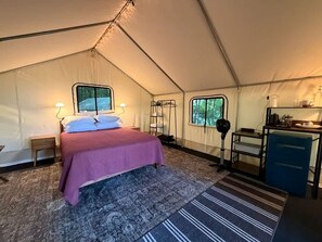 Eine Zelthütte mit Bett, kleinem Tisch, Stuhl, Schreibtisch und Fenster.