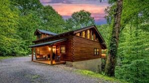 Eine Blockhütte mit Veranda, einer Schotterauffahrt und umgeben von dichtem Wald.