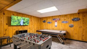 Ein Zimmer mit Kicker, Billardtisch und einem Fernseher, der eine Naturansicht zeigt.