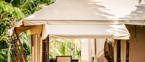 A tented accommodation with a single bed, a table, and a chair.