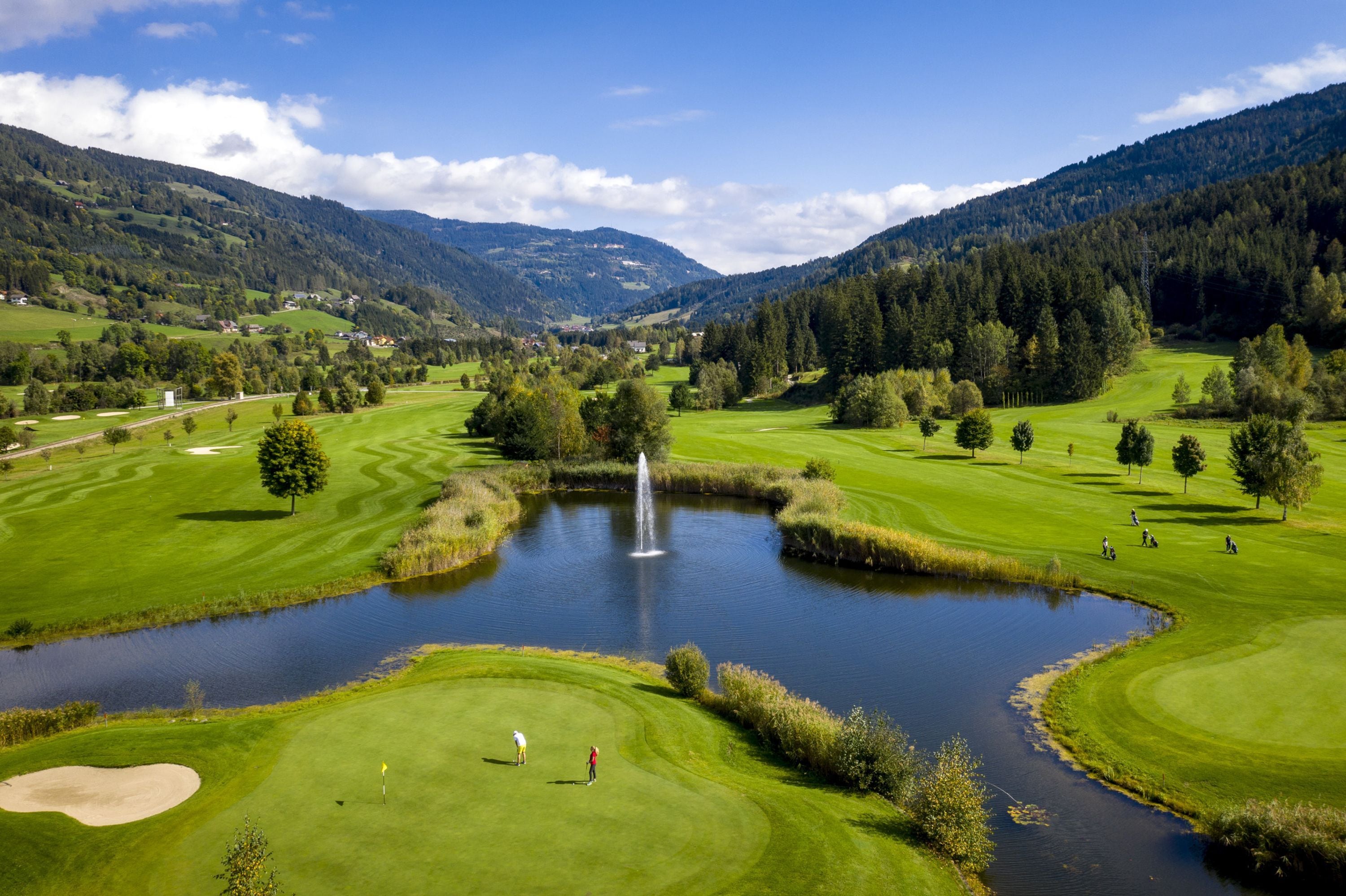 A golf course with a pond, trees, and mountains in the background.
