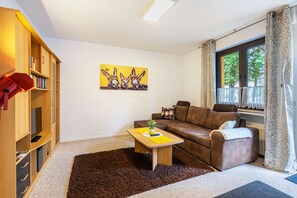 A living room with a brown sofa, a coffee table, a bookshelf, and a painting of donkeys. - Holiday Apartment 'Eselei' with Shared Garden and Wi-Fi (Belm)