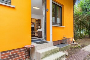 Ein gelbes Gebäude mit Ziegelgrund, einer Treppe zum Eingang und einem kleinen Tisch vor der Tür.