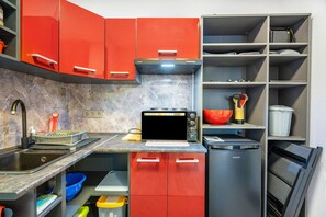 Une cuisine avec des placards rouges, un four à micro-ondes, un évier et divers ustensiles.
