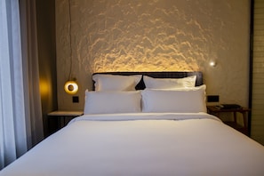 Una cama bien tendida con sábanas blancas en una habitación con pared texturizada y una lámpara circular.