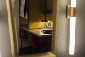 Habitación de hotel compacta con escritorio, silla, lámpara y espejo.