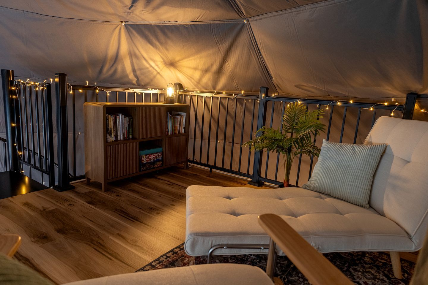 A tent interior with a sofa, bookshelf, and string lights.