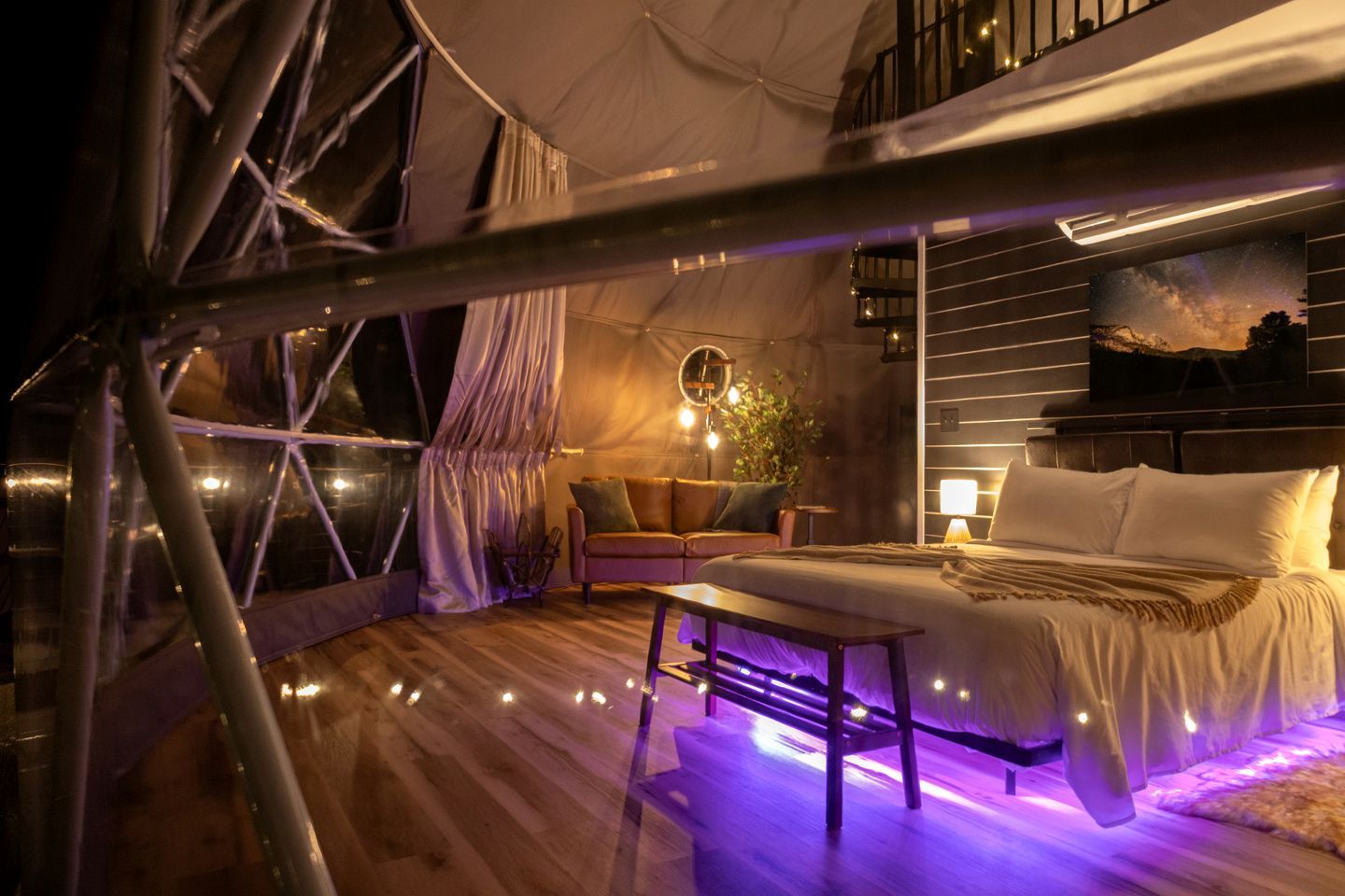 A tented accommodation with a bed, seating area, and a view of the night sky.