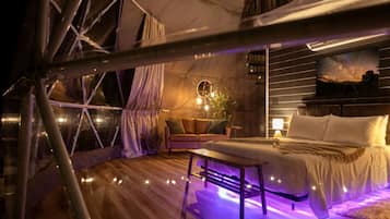 A tented accommodation with a bed, seating area, and a view of the night sky.