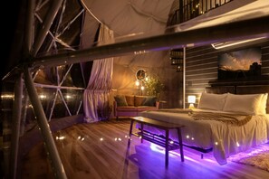 Alojamiento en tienda de campaña con cama, zona de estar y vistas al cielo nocturno.